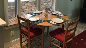A dining area with a stone wall, a table set for four, and a view of trees through large windows. - You will love our beautifully furnished cottage in the woods (Shingletown)