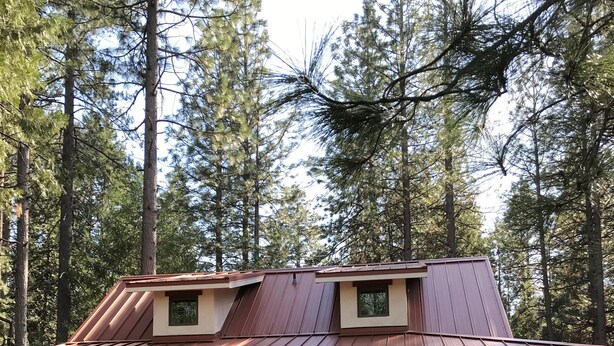 A two-story building with a metal roof, stone foundation, and large windows. - You will love our beautifully furnished cottage in the woods (Shingletown)