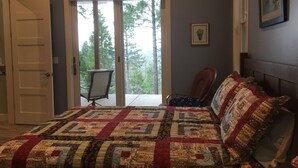A bedroom with a large bed, a chair, and a door leading to a balcony. - You will love our beautifully furnished cottage in the woods (Shingletown)