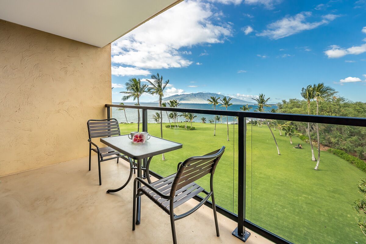 Ein Balkon mit Tisch und Stühlen, der auf eine gepflegte Rasenfläche und ein fernes Gebirge blickt.