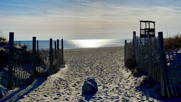 A sandy beach with a wooden fence and a rock in the center. - Breezy Vibes Cottage (3bd) ~ Backyard Blissful  ~ Walk to beaches (South Yarmouth)