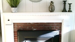 A fireplace with a brick surround, a white mantel, and a green clock above it. - Breezy Vibes Cottage (3bd) ~ Backyard Blissful  ~ Walk to beaches (South Yarmouth)