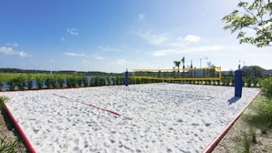 A sandy beach volleyball court with a net, surrounded by greenery and a clear sky.