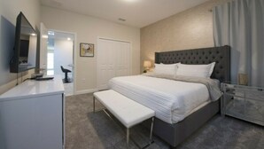 A bedroom with a large bed, a bench, a desk, a mirror, and a bedside table.