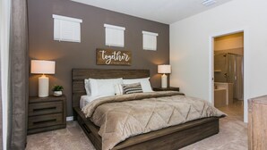 A bedroom with a large bed, two bedside tables with lamps, a wall-mounted sign, and a door leading to a bathroom. - Fabulous Single Home w/ Pool at Solterra Resort (Davenport)