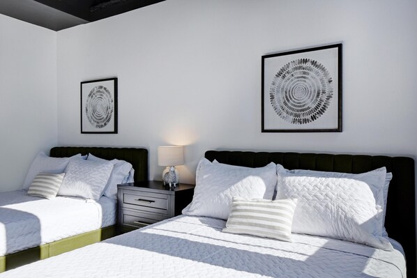 A modern bedroom with two beds, a nightstand, and two framed artworks on the wall.