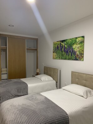 A hotel room with two beds, a wardrobe, and a painting of flowers on the wall.