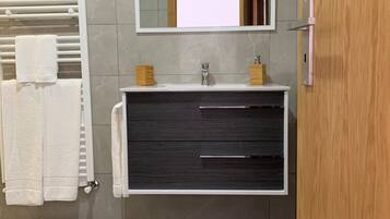 Un baño moderno con pared de azulejos de mármol, toallero blanco, tocador de madera oscura con espejo y una alfombra marrón.