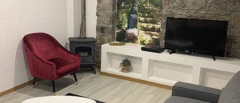 Una sala de estar con pared de piedra, chimenea, televisor, sillón rojo y sofá gris.