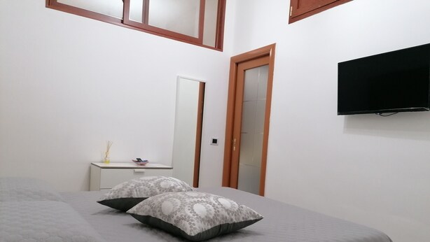 A bedroom with a bed, two pillows, a bedside table, a mirror, a wardrobe, and a TV mounted on the wall. - Stay in the heart of the historic center of Bari (Bari)