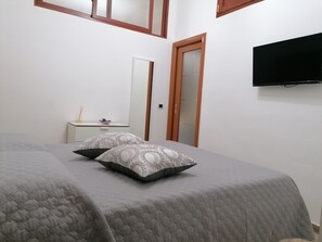A bedroom with a bed, two pillows, a bedside table, a mirror, a wardrobe, and a TV mounted on the wall.