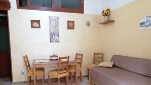 A cozy room with a wooden dining table, four chairs, a sofa, and a small shelf with a vase of sunflowers. - Stay in the heart of the historic center of Bari (Bari)