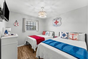 Une chambre avec deux lits, une télévision, une fenêtre, un gilet de sauvetage et un panneau indiquant la présence d’une patrouille de surveillance de la plage.