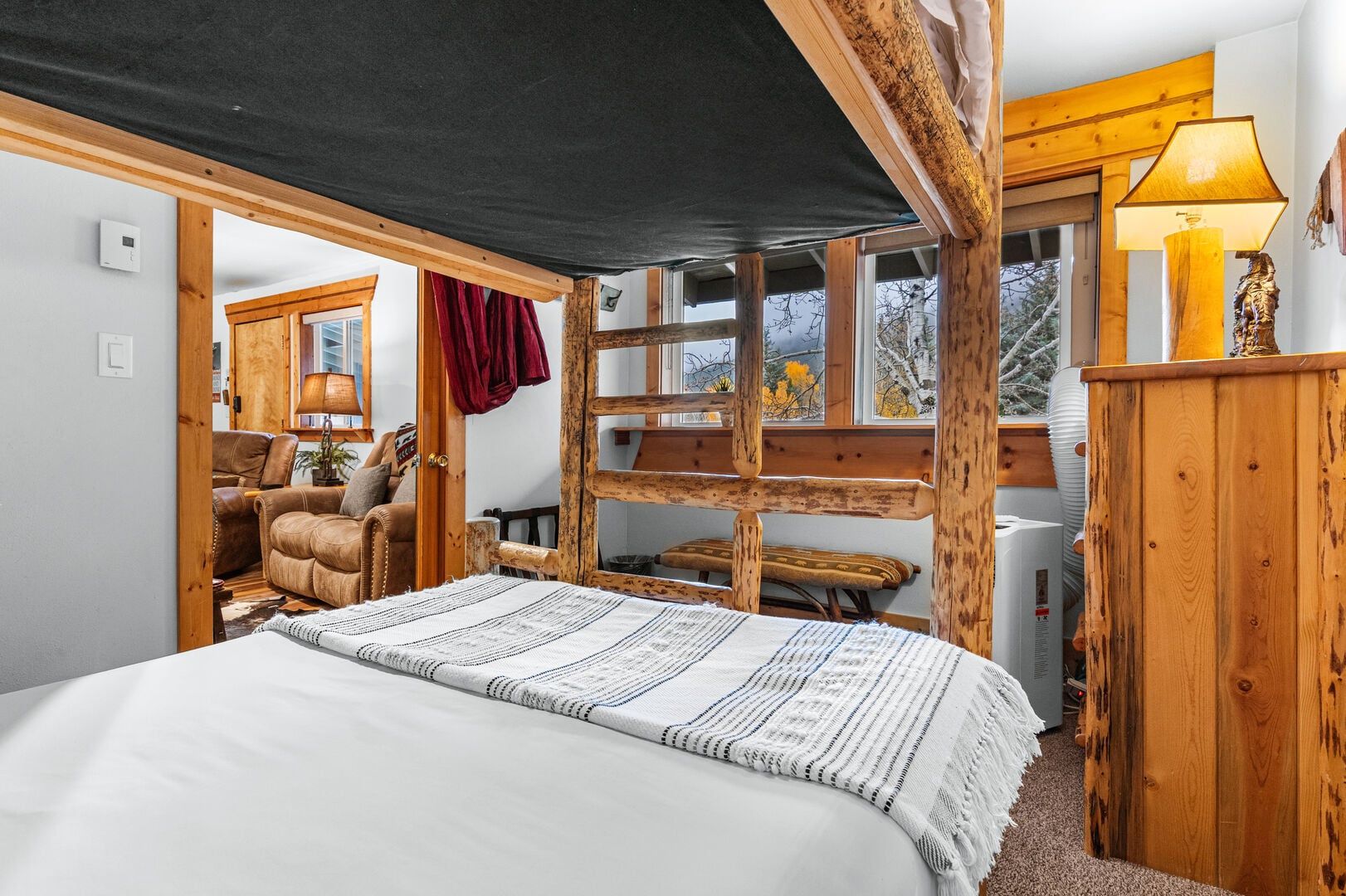 A bedroom with a large bed, wooden headboard, and a window with a view of trees.
