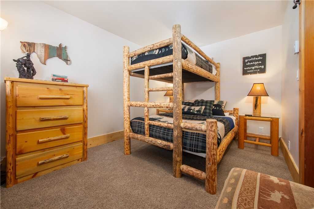 Ein Stockbett mit Holzrahmen, eine Kommode mit mehreren Schubladen, ein kleiner Tisch mit Lampe und ein motivierendes Wandbild.