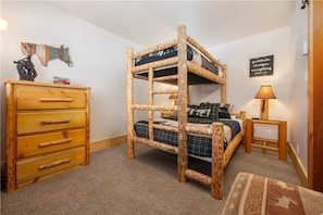Una cama litera con estructura de madera, un aparador con varios cajones, una mesita de noche con una lámpara y un letrero motivacional en la pared.