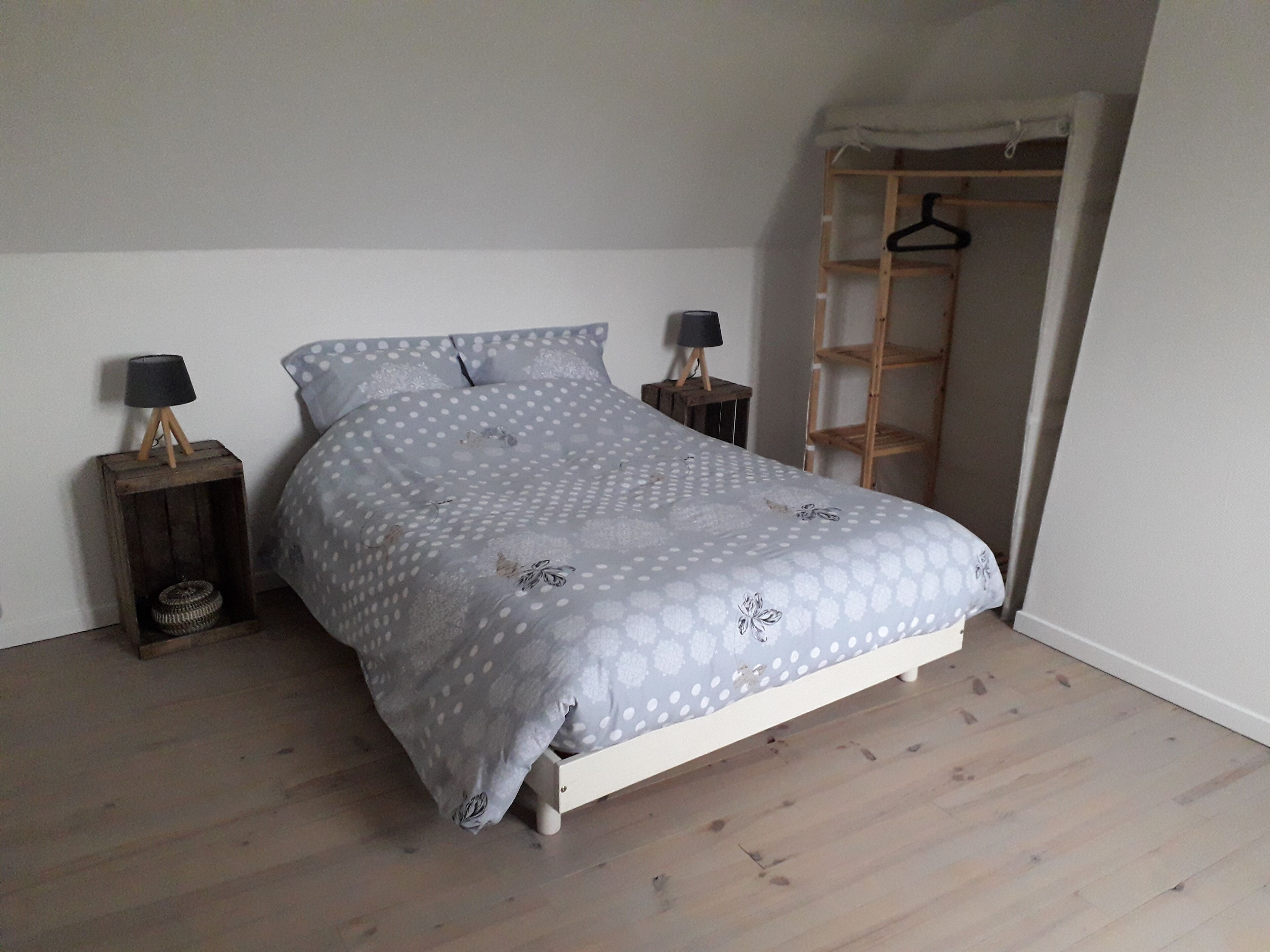 A bedroom with a bed, two bedside tables, a small lamp on each table, a wooden floor, and a wooden wardrobe with a ladder.