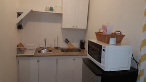 Cocina compacta con armarios blancos, microondas, pileta y una pequeña mesada.