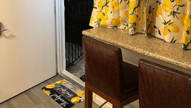 Una habitación con una puerta, un banco, una alfombra pequeña y un cortinero con estampado de limón.