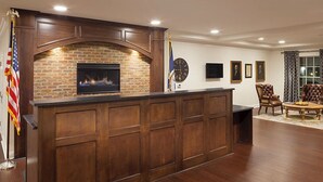 A wooden reception desk with a brick fireplace, a clock, and framed pictures on the wall.