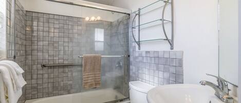 Un bagno con doccia vetrata, un water bianco e un lavandino con specchio.