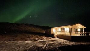 A building with a porch and a staircase leading up to the entrance, situated on a snowy landscape with a clear night sky. - EYVÍK Cottage #2 on the Golden Circle (Selfoss)