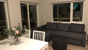 A modern living room with a grey sofa, a white table, and a vase with flowers.