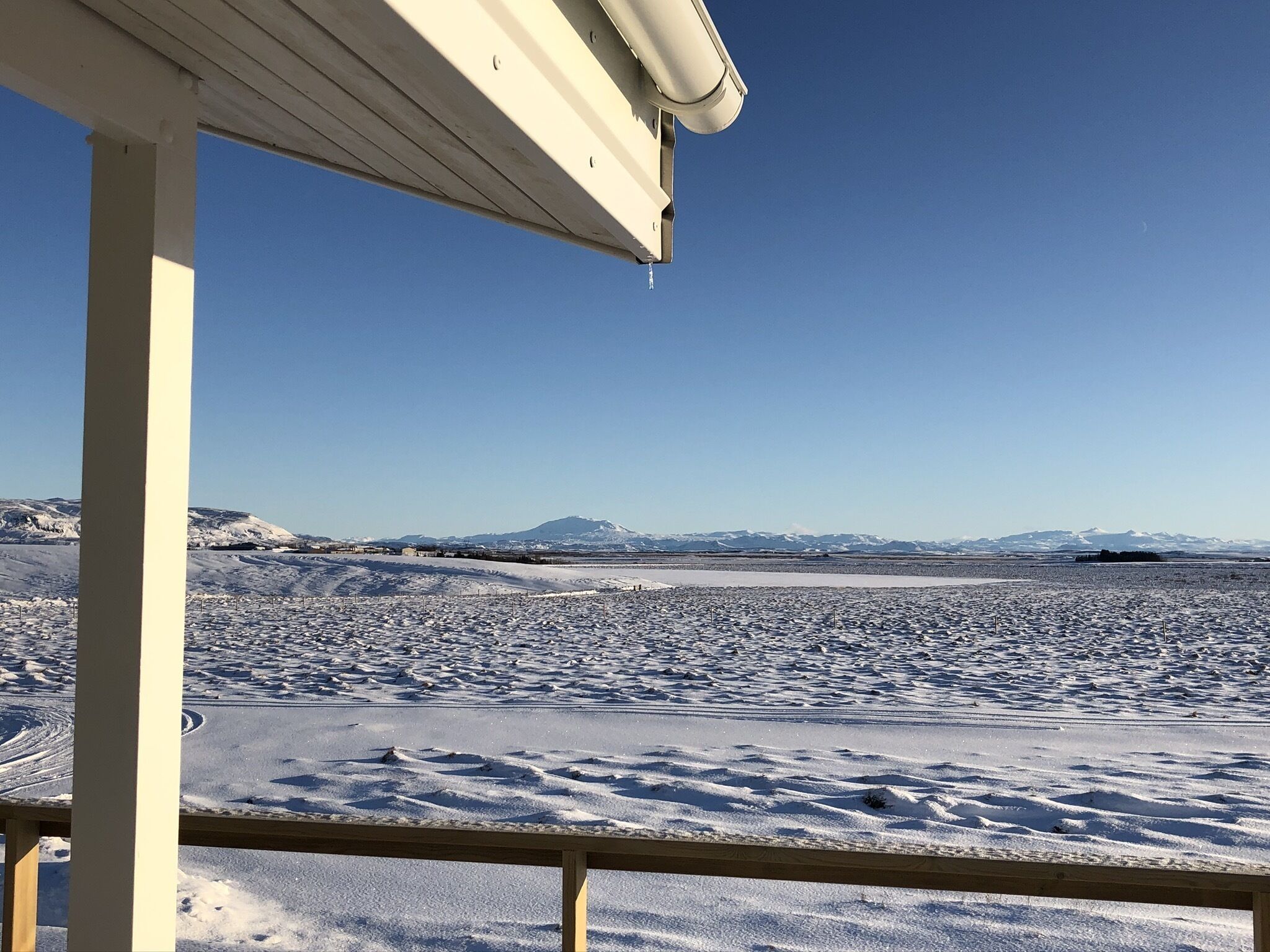 A snowy landscape with a clear sky, a wooden structure, and distant mountains.
