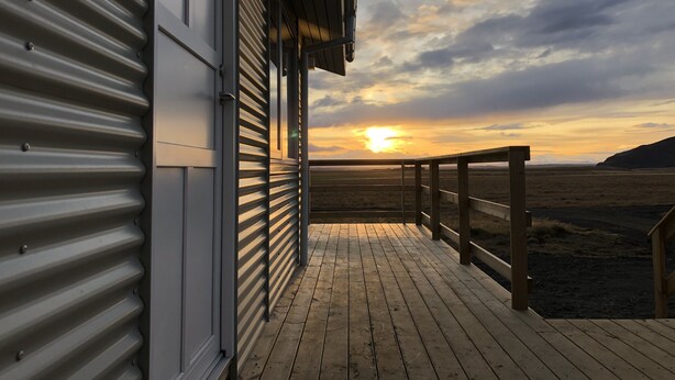 A wooden deck with a metal railing, leading to a building with a corrugated metal exterior.