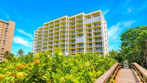 Un hôtel à plusieurs étages, doté de balcons, entouré d’une végétation luxuriante et agrémenté d’une promenade en bois.