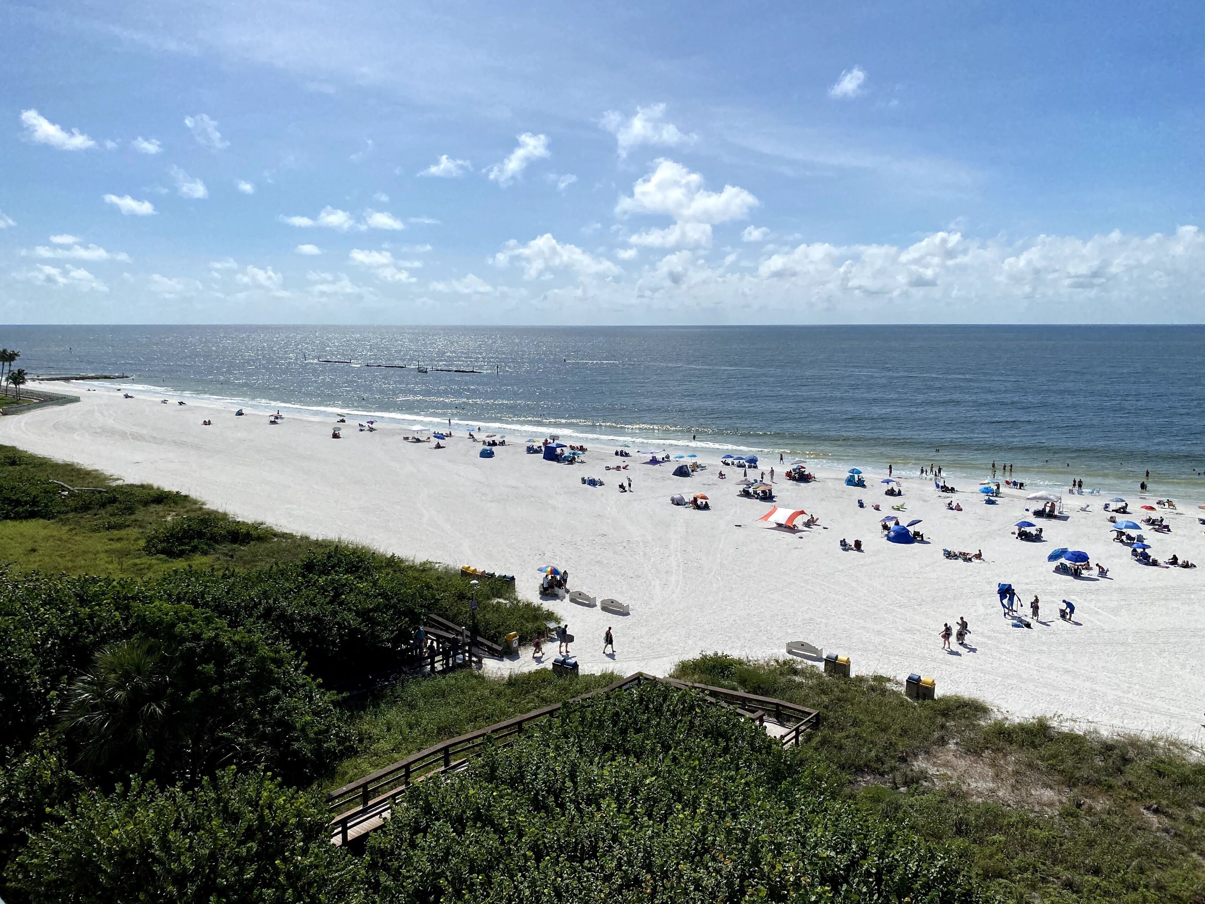 A beach with white sand, clear blue sky, and a few people.