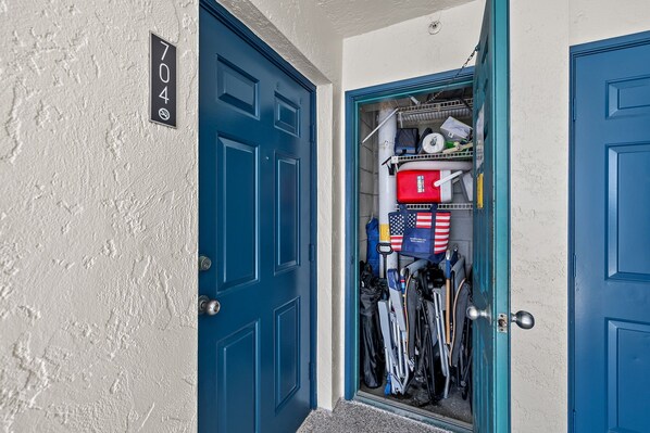 A blue door with a house number 704, leading to a storage area with skis, a red suitcase, and an American flag.
