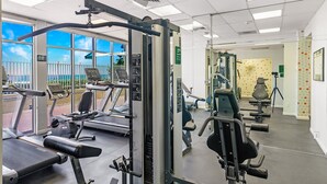 Une salle de sport équipée de tapis de course, d’appareils de musculation et d’une grande fenêtre donnant sur une clôture et des arbres.