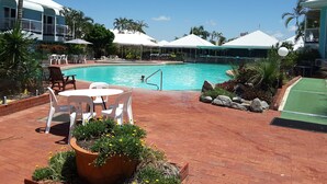 A swimming pool with a person swimming, surrounded by outdoor seating and greenery.