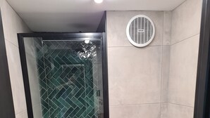 A bathroom with a glass shower enclosure, a toilet, a washing machine, and a yellow rug.