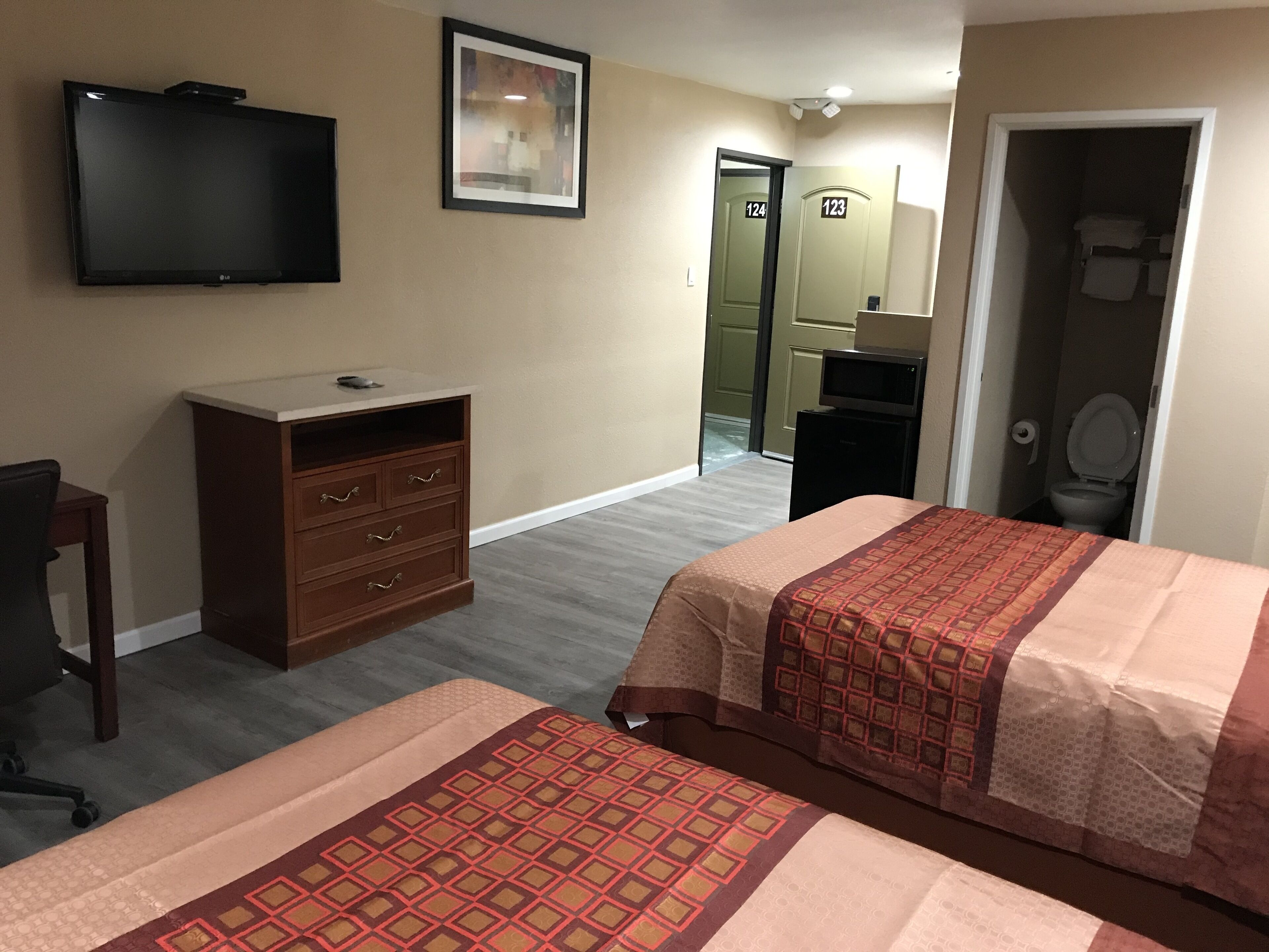 Ein Hotelzimmer mit zwei Betten, einem Fernseher, einem Schminktisch und einer Tür zu einem Badezimmer.