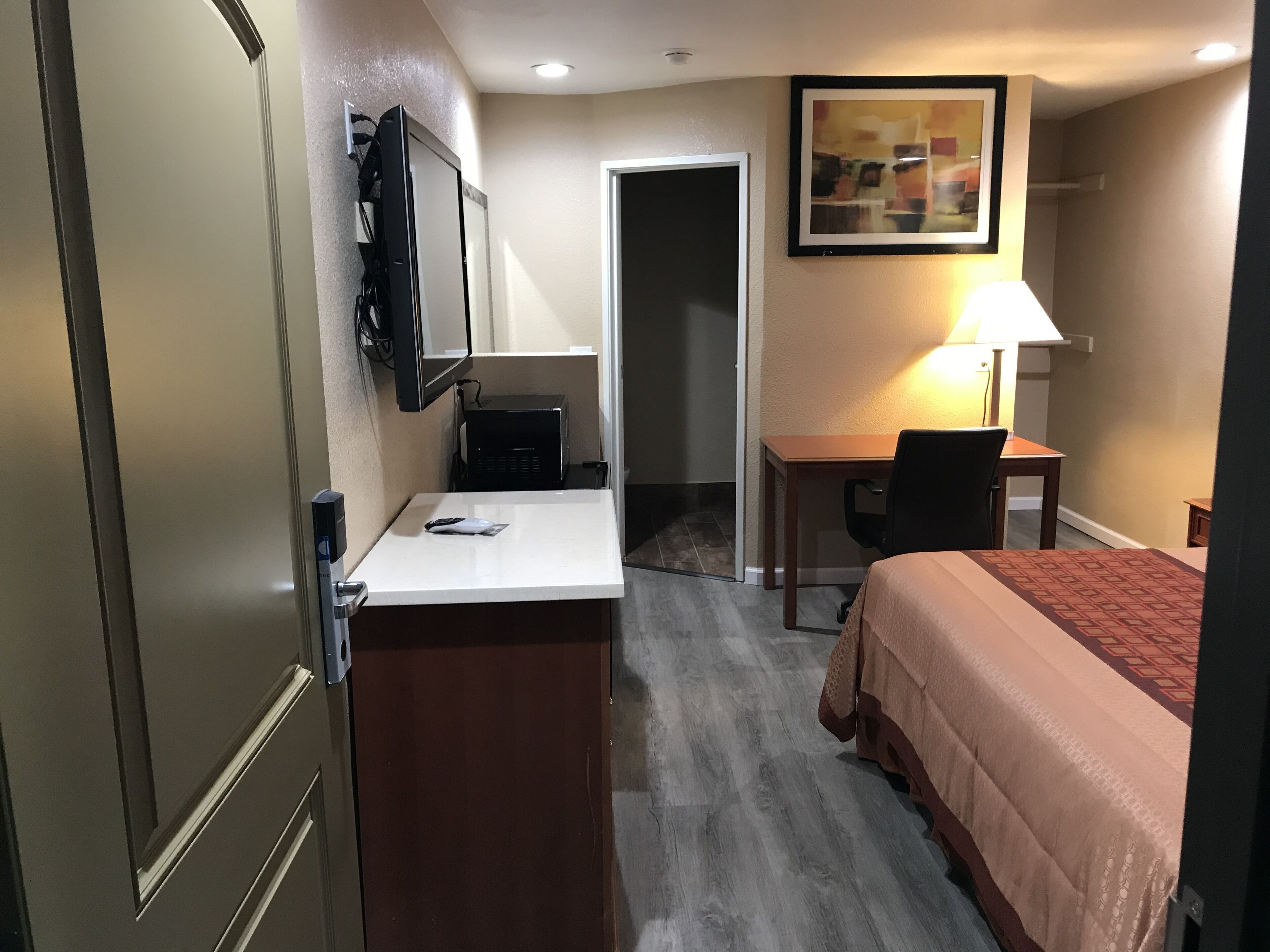 A hotel room with a bed, desk, chair, and a television mounted on the wall.