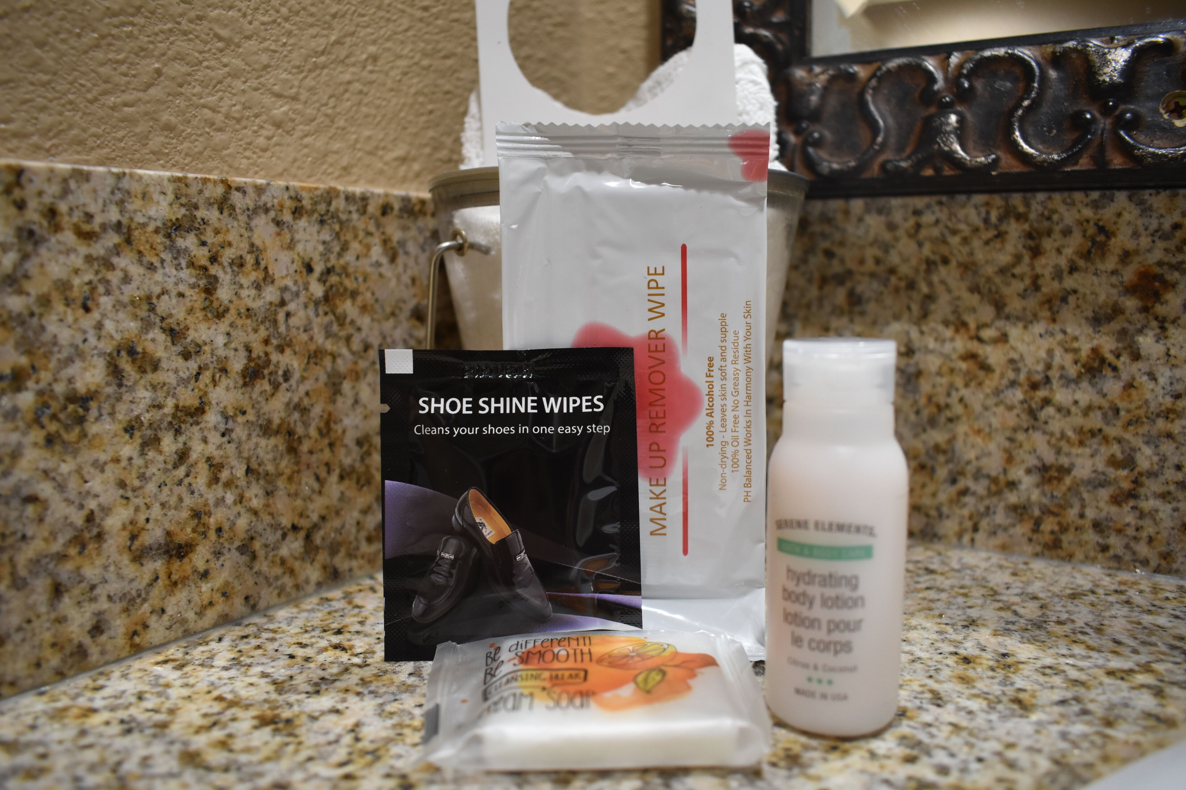 A countertop with a shoe shine kit, a makeup remover wipe, a cream soap, and a hydrating lotion.