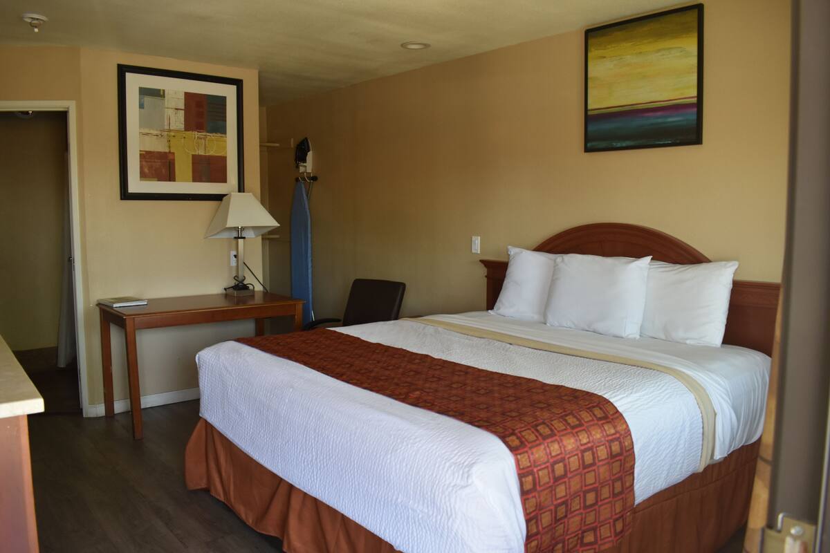 A hotel room with a large bed, a desk, a chair, and two paintings on the walls.
