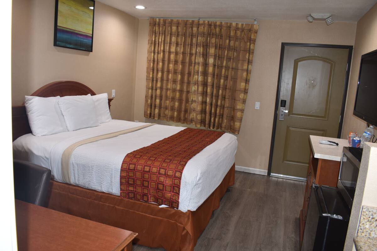 A hotel room with a bed, a desk, a television, and a door.