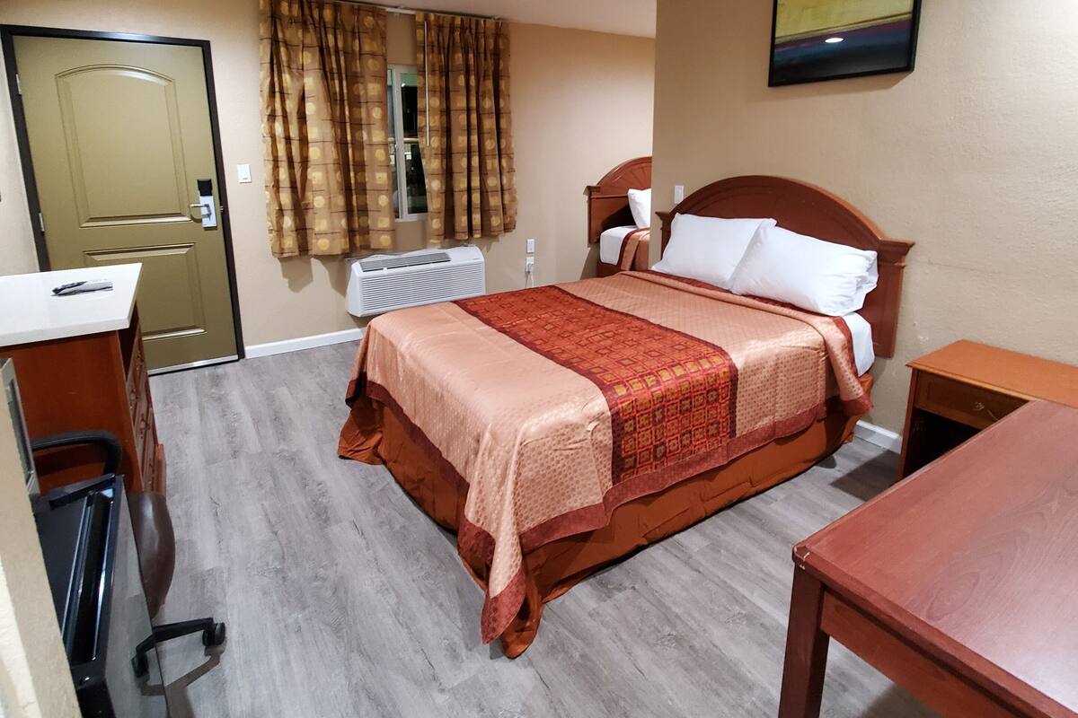 A hotel room with a bed, a desk, a chair, a table, a door, and a window with curtains.