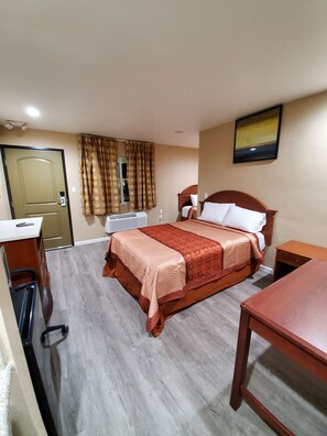 A hotel room with a bed, a desk, a chair, a table, a door, and a window with curtains.