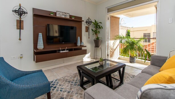 Ein Wohnzimmer mit Flachbildfernseher, einer Couch, einem Couchtisch und einem Balkon mit Blumentöpfen.