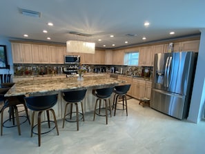 A modern kitchen with a granite countertop, stainless steel appliances, and wooden bar stools. - Night jasmine oceanfront vacation house (Cudjoe Key)