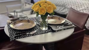 Een eettafel gedekt met borden, bestek en een vaas met gele bloemen.