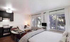 A bedroom with a bed, a desk, a chair, a TV, and a window with curtains.