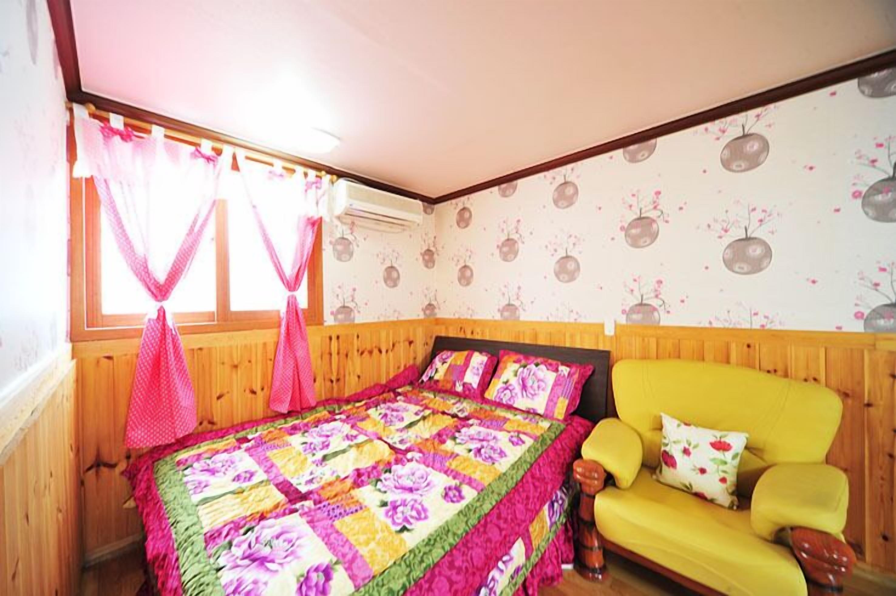 A bedroom with a wooden bed, a yellow sofa, and floral wallpaper.