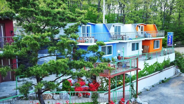 Un immeuble à plusieurs étages doté d’un balcon, entouré de verdure et de fleurs rouges.
