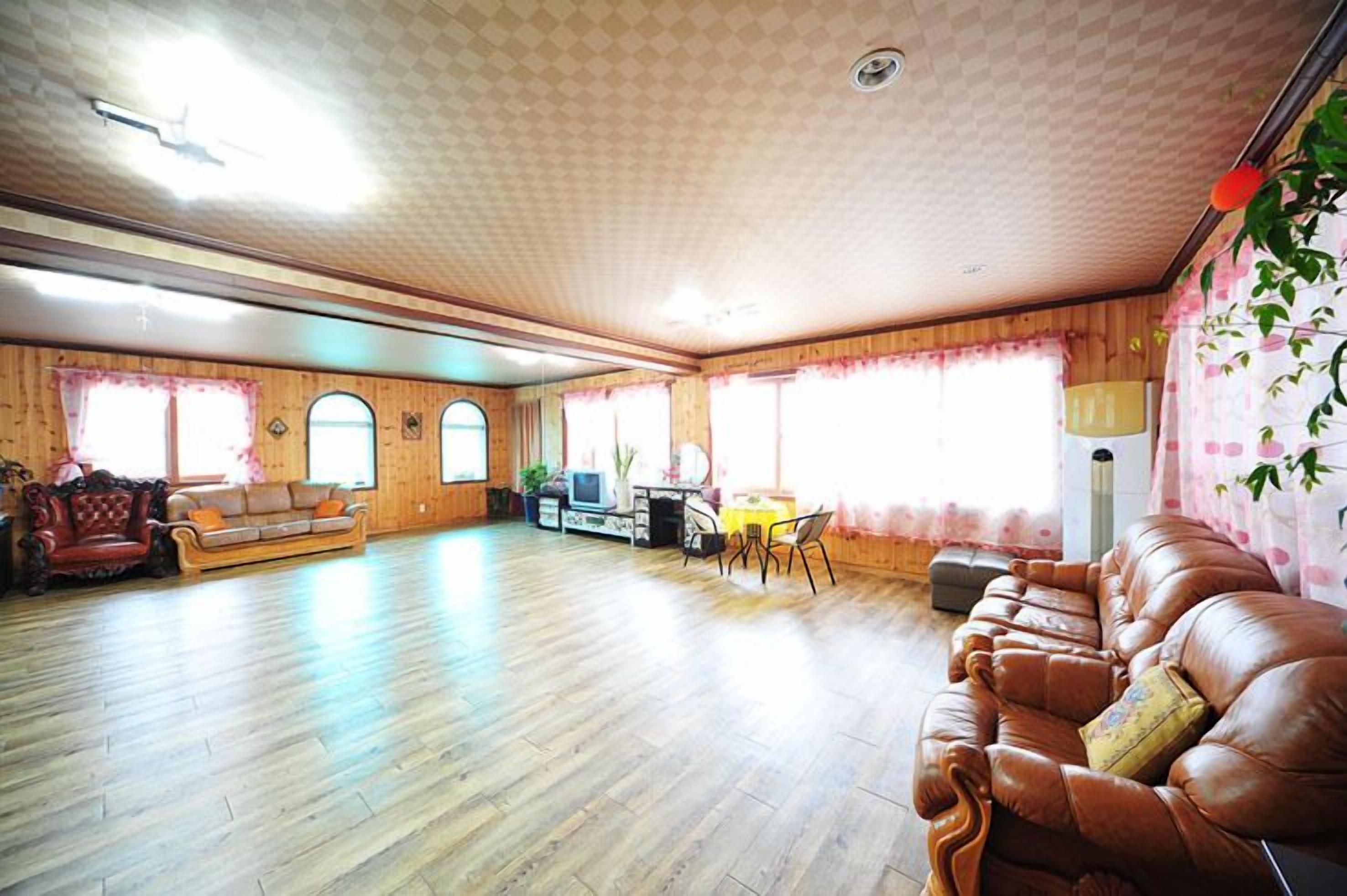 Un salón amplio con suelo de madera, un sofá de cuero marrón, un sillón rojo y un televisor.