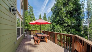 A wooden deck with a picnic table and chairs, surrounded by a wooden railing and dense trees. - Beautiful & Cozy Cabin. Perfect Location, Kid Friendly. Free Starlink WIFI. (Cold Springs)